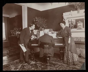 Clara De Regand wijst naar een partituur terwijl een man piano speelt, 1910